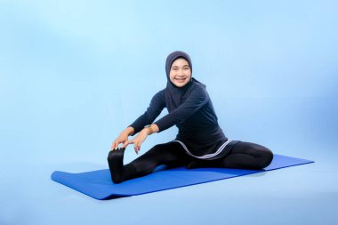 Bir kadın laptopu ve su şişesi olan bir minderde yoga yapıyor. Gülümsüyor ve antrenmanından zevk alıyor.