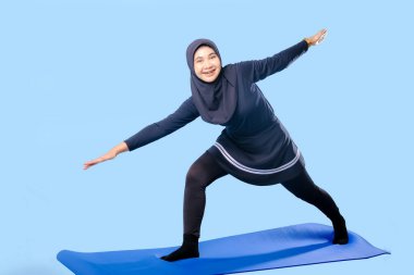 Bir kadın laptopu ve su şişesi olan bir minderde yoga yapıyor. Gülümsüyor ve antrenmanından zevk alıyor.