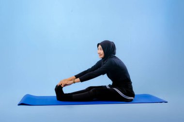 Bir kadın laptopu ve su şişesi olan bir minderde yoga yapıyor. Gülümsüyor ve antrenmanından zevk alıyor.