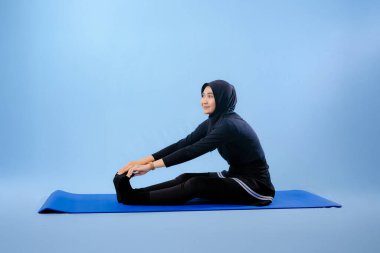 Bir kadın laptopu ve su şişesi olan bir minderde yoga yapıyor. Gülümsüyor ve antrenmanından zevk alıyor.