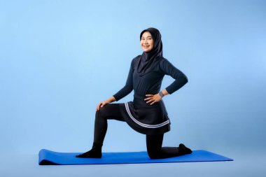 Bir kadın laptopu ve su şişesi olan bir minderde yoga yapıyor. Gülümsüyor ve antrenmanından zevk alıyor.