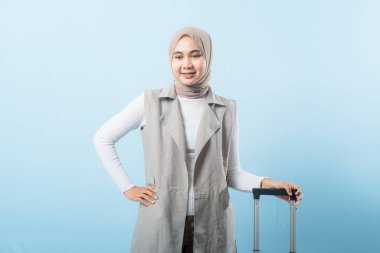 Gri yelek ve beyaz gömlek giyen bir kadın bir bavul tutuyor. Gülümsüyor ve mutlu.