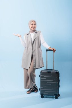 Bir kadın bavuluyla poz veriyor, gülümsüyor ve elini kaldırıyor. Macera ve heyecan kavramı, kadın bir yolculuğa çıkmaya hazır.