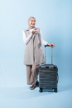 Bir kadın bavuluyla poz veriyor, gülümsüyor ve elini kaldırıyor. Macera ve heyecan kavramı, kadın bir yolculuğa çıkmaya hazır.