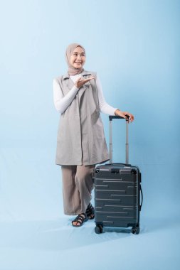 Bir kadın bavuluyla poz veriyor, gülümsüyor ve elini kaldırıyor. Macera ve heyecan kavramı, kadın bir yolculuğa çıkmaya hazır.