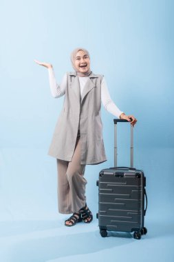 Bir kadın bavuluyla poz veriyor, gülümsüyor ve elini kaldırıyor. Macera ve heyecan kavramı, kadın bir yolculuğa çıkmaya hazır.