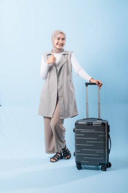 Bir kadın bavuluyla poz veriyor, baş parmağını kaldırıyor. Heyecan ve macera kavramı, kadın bir yolculuğa çıkmaya hazır.