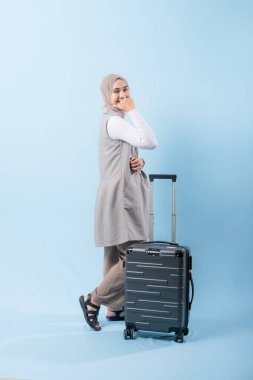 Bir kadın bavuluyla poz veriyor, gülümsüyor ve elini kaldırıyor. Macera ve heyecan kavramı, kadın bir yolculuğa çıkmaya hazır.