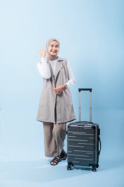 Bir kadın bavuluyla poz veriyor, gülümsüyor ve elini kaldırıyor. Macera ve heyecan kavramı, kadın bir yolculuğa çıkmaya hazır.