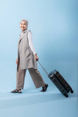 Bir kadın bavuluyla poz veriyor, gülümsüyor ve mutlu görünüyor. Bavul siyah ve tekerlekleri var. Bu da taşımayı kolaylaştırıyor. Macera ve heyecan kavramı, kadın bir yolculuğa çıkmaya hazır.