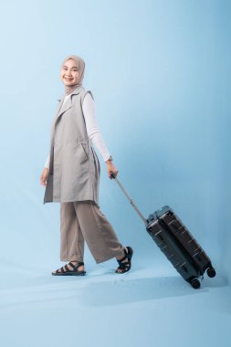 Bir kadın bavuluyla poz veriyor, gülümsüyor ve mutlu görünüyor. Bavul siyah ve tekerlekleri var. Bu da taşımayı kolaylaştırıyor. Macera ve heyecan kavramı, kadın bir yolculuğa çıkmaya hazır.