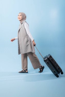 Bir kadın bavuluyla poz veriyor, gülümsüyor ve mutlu görünüyor. Bavul siyah ve tekerlekleri var. Bu da taşımayı kolaylaştırıyor. Macera ve heyecan kavramı, kadın bir yolculuğa çıkmaya hazır.