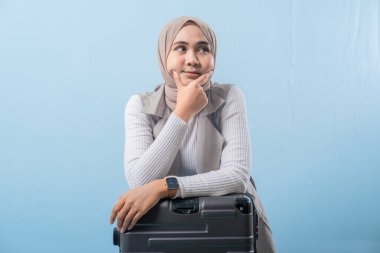 Eşarp takan ve kameraya bakan bir kadın. O bir bavulun üzerinde oturuyor. Derin düşüncelere dalmış.