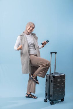 Başörtüsü takan bir kadın bir bavul ve cep telefonuyla yürüyor. O mutlu ve seyahatinin tadını çıkarıyor.