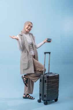 Başörtüsü takan bir kadın bir bavul ve cep telefonuyla yürüyor. O mutlu ve seyahatinin tadını çıkarıyor.