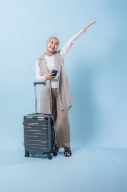 Bir kadın bavulun yanında duruyor ve elinde cep telefonu var. Gülümsüyor ve mutlu.