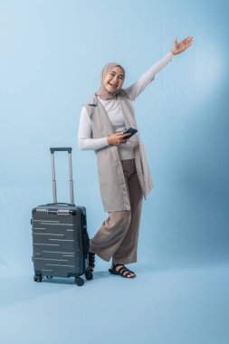 Bir kadın bavulun yanında duruyor ve elinde cep telefonu var. Gülümsüyor ve mutlu.