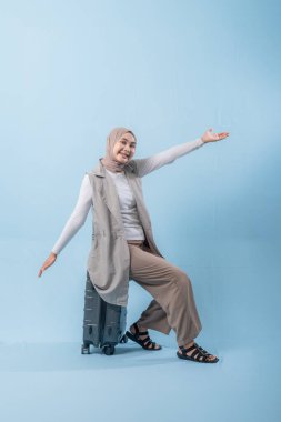 Başörtüsü takan bir kadın bavulla poz veriyor. Gülümsüyor ve mutlu.