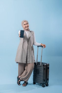 Başörtüsü takan bir kadın cep telefonu tutuyor ve bir bavulun yanında duruyor. Seyahat ve macera kavramı, kadın bir yolculuğa çıkmaya hazırlanırken
