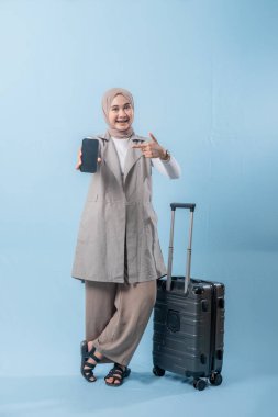 Başörtüsü takan bir kadın cep telefonu tutuyor ve bir bavulun yanında duruyor. Seyahat ve macera kavramı, kadın bir yolculuğa çıkmaya hazırlanırken