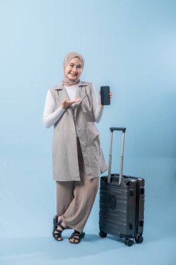 Başörtüsü takan bir kadın cep telefonu tutuyor ve bir bavulun yanında duruyor. Seyahat ve macera kavramı, kadın bir yolculuğa çıkmaya hazırlanırken