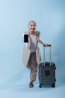 Başörtüsü takan bir kadın cep telefonu tutuyor ve bir bavulun yanında duruyor. Seyahat ve macera kavramı, kadın bir yolculuğa çıkmaya hazırlanırken