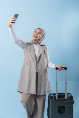 Bir kadın elinde bavul tutarken telefonuyla selfie çekiyor. Seyahat ve macera kavramı, kadın bir yolculuğa çıkmaya hazırlanırken.