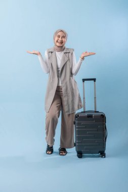 Bir kadın bavulun yanında duruyor, gülümsüyor ve ellerini havaya kaldırıyor. Heyecan ve yolculuk beklentisi.