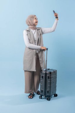 Bir kadın elinde bavul tutarken telefonuyla selfie çekiyor. Seyahat ve macera kavramı, kadın bir yolculuğa çıkmaya hazırlanırken.