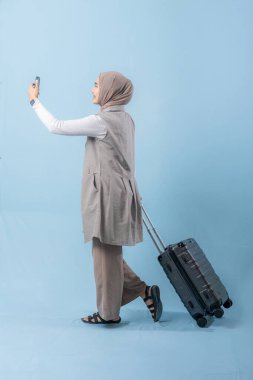 Bir kadın bavuluyla yürüyor ve kendi fotoğrafını çekiyor. Seyahat ve macera kavramı, kadın bir yolculuğa çıkmaya hazırlanırken