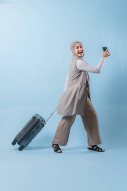 Bir kadın bavuluyla yürüyor ve gülümsüyor. Elinde bir cep telefonu var ve selfie çekiyor. Seyahat ve macera kavramının yanı sıra yeni yerler keşfetme heyecanı.