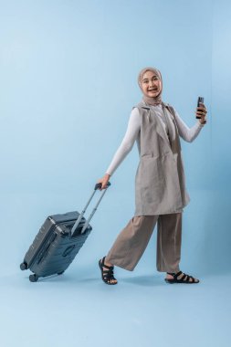 Başörtüsü takan bir kadın bir bavul ve cep telefonuyla yürüyor. O mutlu ve seyahatinin tadını çıkarıyor.