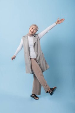 Bronz ceketli ve kahverengi pantolonlu bir kadın gülümsüyor ve kollarını kaldırıyor. Mutluluk ve pozitiflik kavramı