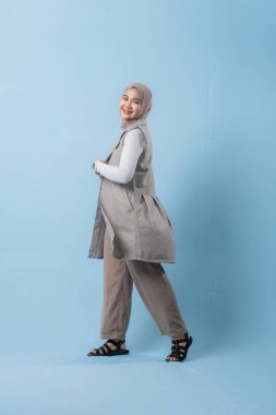 Beyaz gömlek ve ten rengi pantolon giyen bir kadın gülümsüyor ve yürüyor. Eşarp ve sandalet takıyor.