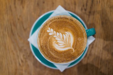 Artistik Kahve Latte ve Karmaşık Yaprak Köpük Tasarımı Tahta Masa Üzerinde Turkuaz Kupa Tasarımı