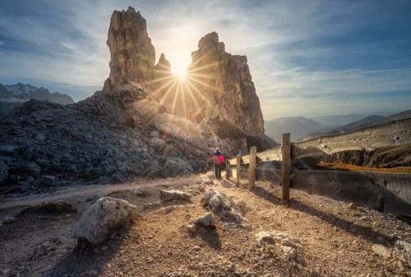 Dolomitler, İtalya 'da sonbaharda günbatımında, dağ yolunda ahşap çitlerin yanında bir kadın ve taşlar. Yoldaki sportif kız ve sonbaharda yüksek kayalar. Kayalıklarla, güneşle, mavi gökyüzüyle renkli bir manzara. Yürüyüş