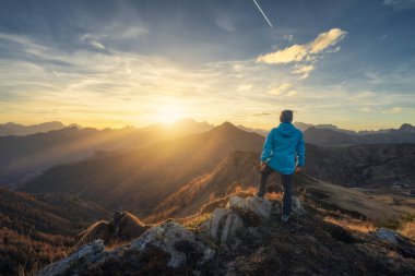 Tepede taş üstündeki adam ve sonbaharda renkli günbatımında sisli güzel dağlar. Dolomitler, İtalya. Sportif adam, sisli dağ sırtları, turuncu çimenler ve ağaçlar, sonbaharda güneşli mavi gökyüzü. Yürüyüş