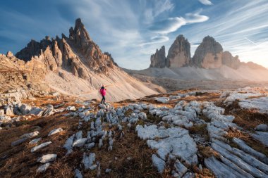 Sonbaharda gün batımında sırtında sırt çantasıyla dağlarda gezen kız. Tre Cime, Dolomitler, İtalya. Genç bir kadınla güzel bir manzara, yüksek kayalar, patika, taşlar, turuncu çimenler, sonbaharda gökyüzü. Yürüyüş