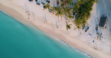 Deniz dalgaları, şemsiyeler, gün batımında kumlu sahilde yeşil palmiyeler. Afrika, Zanzibar 'da yaz. Palmiye ağaçları, insanlar, beyaz kum ve mavi suyla tropik bir manzara. Yukarıdan aşağıya hava manzarası