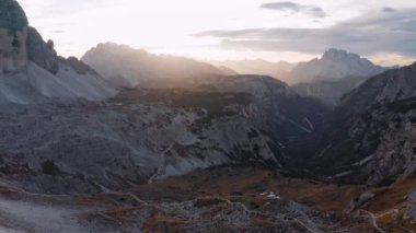 Tre Cime, Dolomitler, İtalya 'da sonbaharda renkli günbatımında kayaların hava manzarası. Renkli manzara. Dağların insansız hava aracı, bulutlu gökyüzü, sonbaharda altın güneş ışığı. Yukarıdan bak. Doğa