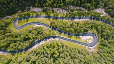 Dolomitler, İtalya 'da yazın güneşli bir günde arabalarla dolambaçlı yol manzarası. Dağ yolundaki trafiğin insansız hava aracı görüntüsü, Avrupa 'daki yeşil ağaçlar ve dağlık çayırlar. Otobanın yukarıdan aşağı görünümü