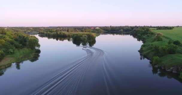 夏の日没時に川で浮遊ボートや水上スキーの空中ビュー モーターボート 青い水 緑の木々や牧草地 ウクライナの川の湾の無人機からのトップビュー 極端なスポーツだ レジャー — ストック動画