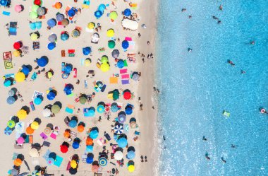 Kumlu sahildeki renkli şemsiyelerin havadan görünüşü, yazın günbatımında mavi denizde yüzen insanlar, İtalya, Sardunya 'da. Turkuaz şeffaf suyu olan tropik bir manzara. Seyahat ve tatil. Üst görünüm
