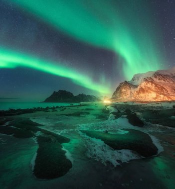 Aurora borealis above Uttakleiv beach in Lofoten islands, Norway. Beautiful northern lights in winter. Starry sky with polar lights. Night landscape with aurora, sea coast, stones, snowy mountains