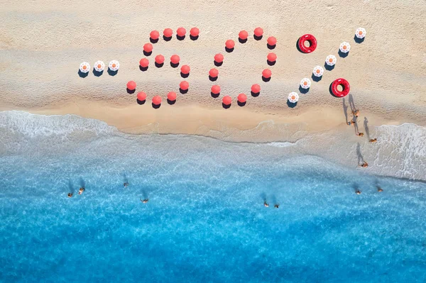 Creative text - 50 percent made from colorful umbrellas on sandy beach and blue sea with waves at sunny day. Aerial view of sea coast and text. Summer sale and discount. Background. Top view