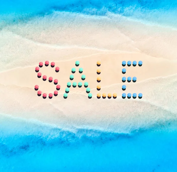 Creative text made from umbrellas on empty sandy beach and blue sea at sunny day. Aerial view of sea coast and text. Summer sale and discount. Background. Top view from drone of clear water, sandbank