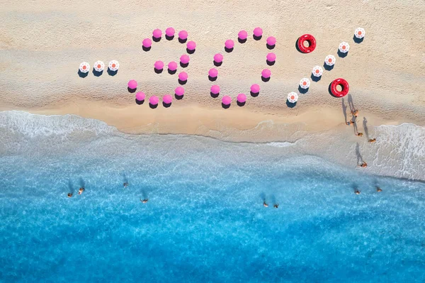 Creative text -30 made from colorful umbrellas on sandy beach and blue sea with waves at sunny day. Aerial view of sea coast and text. Summer sale and discount. Background. Top view of clear water