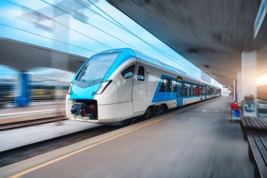 Blue high speed train in motion on the railway station at sunset. Fast modern intercity train and blurred background. Railway platform. Railroad in Slovenia. Commercial and passenger transportation