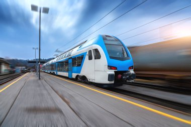 Blue high speed train in motion on the railway station at sunset. Fast modern intercity train and blurred background. Railway platform. Railroad in Slovenia. Commercial and passenger transportation