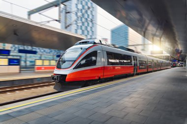 Red high speed train in motion on the railway station at sunset. Fast modern intercity train and blurred background. Railway platform. Railroad in Austria. Commercial and passenger transportation